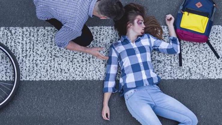 A man checking on a woman who has been hit by a car lying on the road