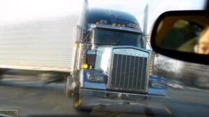 A truck rapidly heading towards a car on the road.
